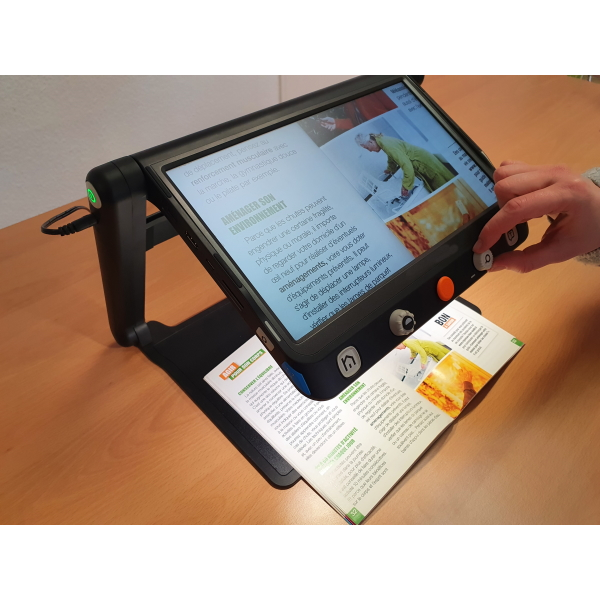 Utilisation de la loupe électronique sur socle surélevé permettant d'avoir en-dessous un article qu'une personne lit.