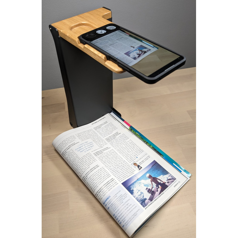 La machine à lire tactile a un format similaire à un smartphone. La photo la présente posée sur un support permettant de facilitant la lecture du magazine posé dessous
