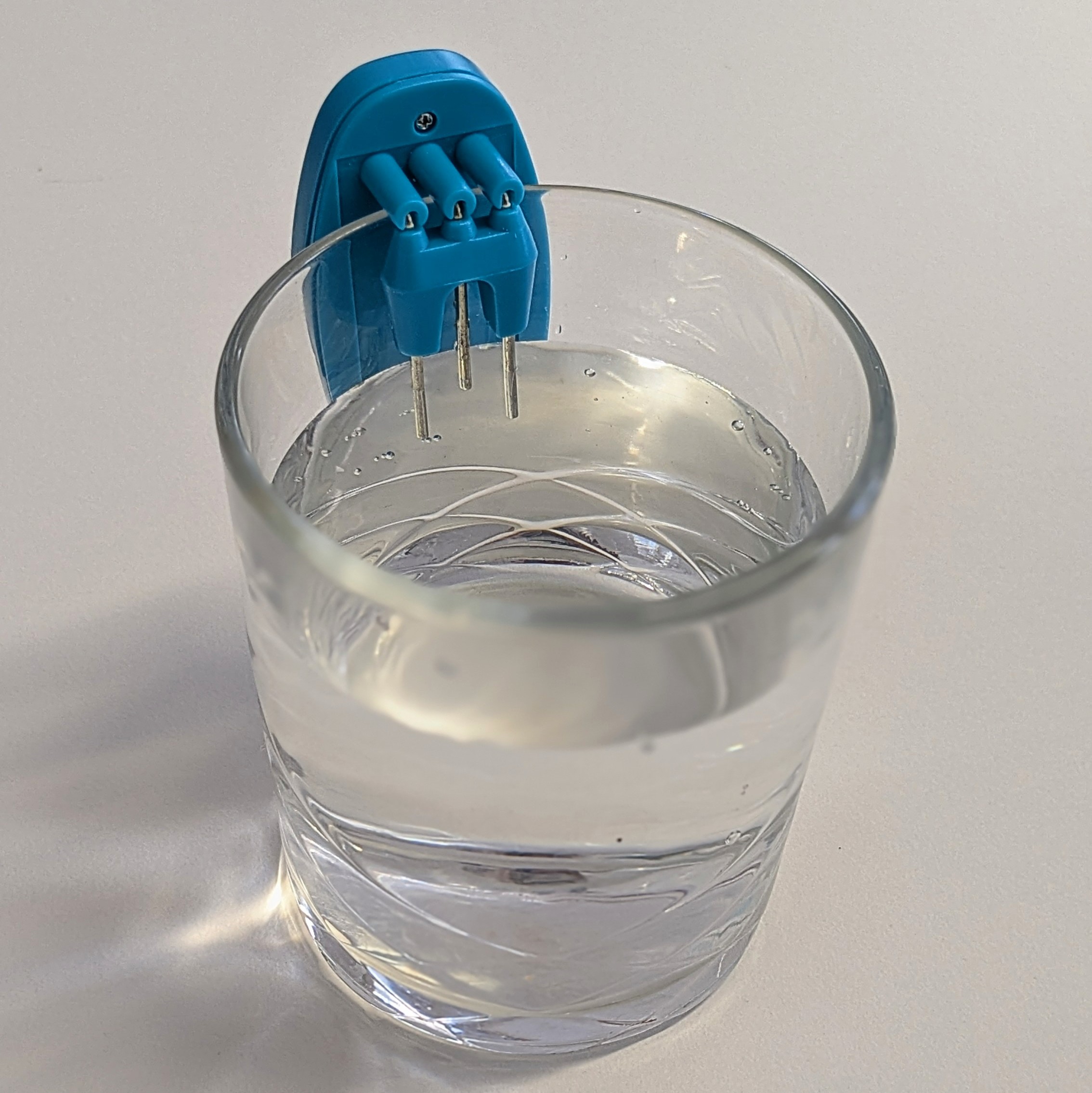 Verre d'eau avec l'indicateur de liquide glisser sur le rebord. Le liquide contenu dans le verre atteint les sondes qui permettent de détecter le niveau maximal.