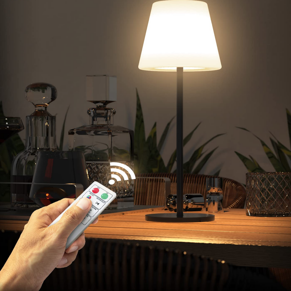 Lampe sur pied placée sur une table de salon avec une main tenant une télécommande munie d'un bouton rouge à gauche, un bouton vert à droit et d'autres boutons poussoirs par-dessous le pouce tenant la télécommande.