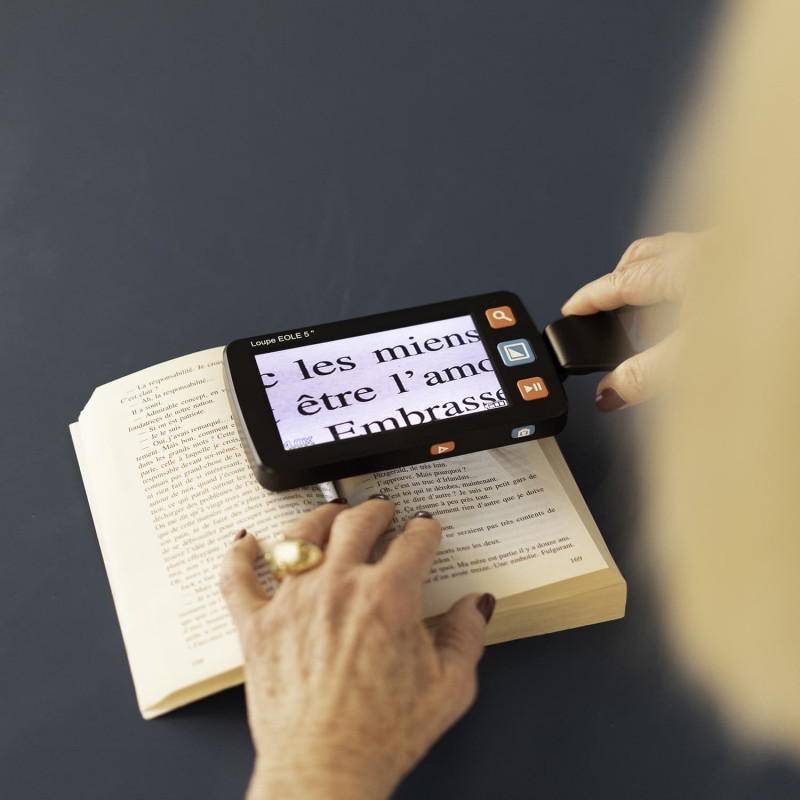 Loupe électronique portable allumée et tenue d'une main par une personne qui lit un livre.