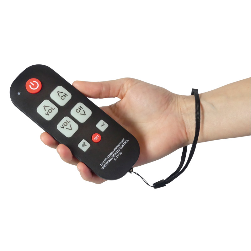Personne qui tient dans sa main une télécommande simplifiée équipée d'une dragonne portée au poignet. Elle a 8 boutons en reliefs et contrastés dont un pour allumer/éteindre, 2 boutons pour le volume, 2 boutons pour les chaines et un pour un accès au menu.