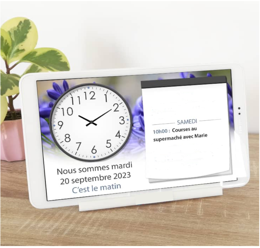 Tablette posée sur un meuble. A gauche de l'écran il y a une horloge indiquant 10h10 et en dessous il y a un texte : Nous sommes mardi 20 septembre 2023, c'est le matin. A droite il y a une partie agenda indiquant un rappel : Samedi à 10h00, courses au supermarché avec Marie.